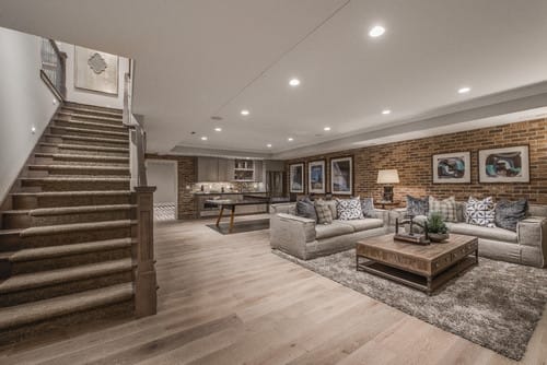 Spacious finished basement with exposed brick wall, hardwood floors, comfortable seating area, and a wet bar